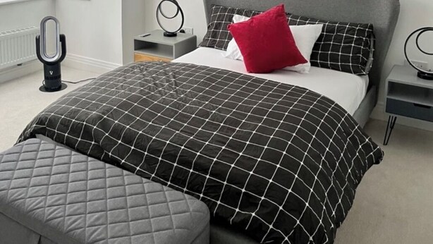 Quarto com cama, mesas de cabeceira, luminária na parede e janela com persianas.