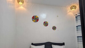 A bedroom with a bed, white walls, and three wall-mounted light fixtures. - Idembe Heritage (Nyamabuye)