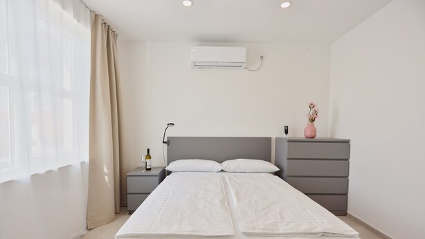 Una habitación de hotel moderna con cama, mesitas de noche, cómoda y aire acondicionado, además de una ventana con cortinas.