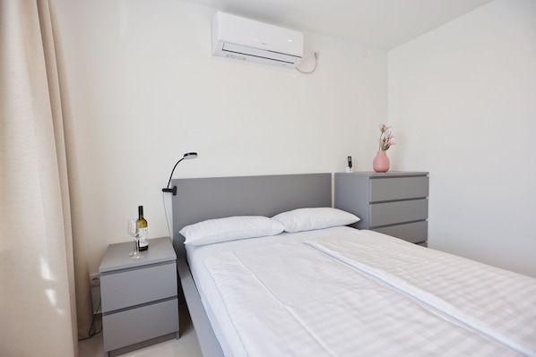 Ein Hotelzimmer mit Bett, Nachttisch, Lampe, Klimaanlage und einer Blumenvase.