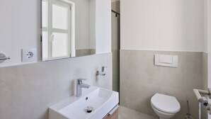 Un baño moderno con lavamanos, espejo y retrete blancos.