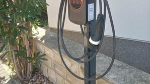Una estación de carga para vehículos eléctricos con pantalla digital, un cable y un botón rojo.