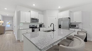 A modern kitchen with white cabinets, granite countertops, a stainless steel refrigerator, and a built-in microwave. - Fully-Fenced Backyard! Perfect for Families/Groups (Tallahassee)