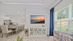 A modern living room with a dining area, a white cabinet, a flat-screen TV, and a large window with blinds. - Fully-Fenced Backyard! Perfect for Families/Groups (Tallahassee)