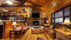 A cozy cabin interior with a stone fireplace, wooden furniture, and a kitchen area. - Trails End Lodge - 5 BR cabin in Morganton with Games, WiFi, Hot Tub (Morganton)