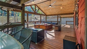 An outdoor deck with wooden flooring, wicker furniture, a ceiling fan, and a hot tub. - Trails End Lodge - 5 BR cabin in Morganton with Games, WiFi, Hot Tub (Morganton)