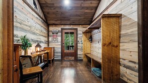 A wooden interior with a wooden bench, a table with a plant, and a door with a 'Please' sign. - Trails End Lodge - 5 BR cabin in Morganton with Games, WiFi, Hot Tub (Morganton)