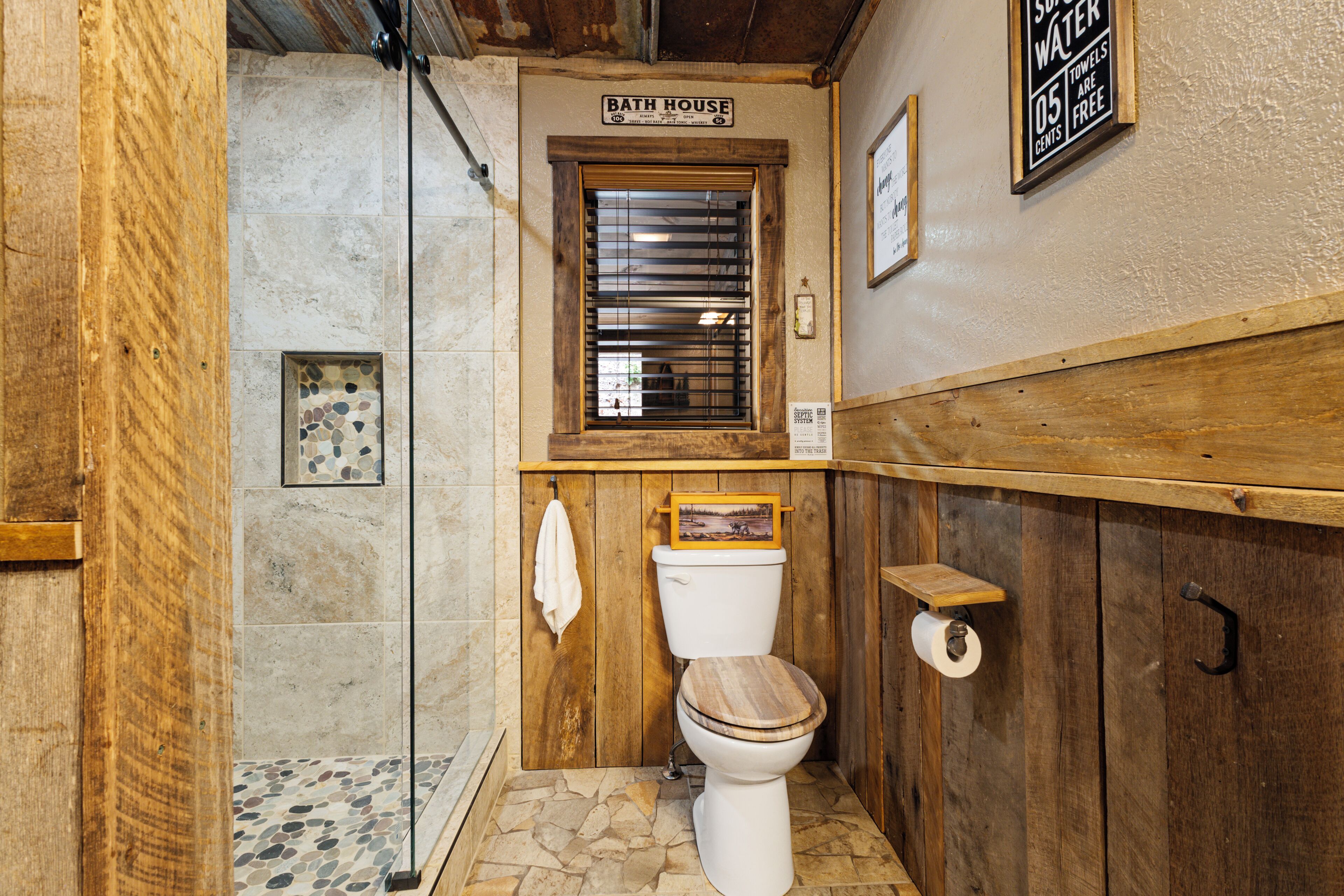Une salle de bain avec un meuble-lavabo en bois, des toilettes avec un abattant en bois, un espace douche et un panneau indiquant que des serviettes sont mises à disposition gratuitement.
