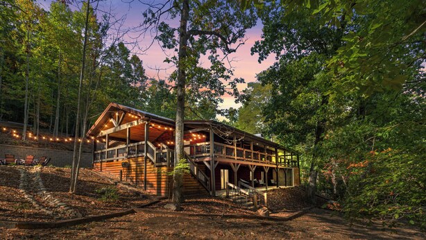 A wooden cabin with a deck and stairs, surrounded by trees. - Trails End Lodge - 5 BR cabin in Morganton with Games, WiFi, Hot Tub (Morganton)