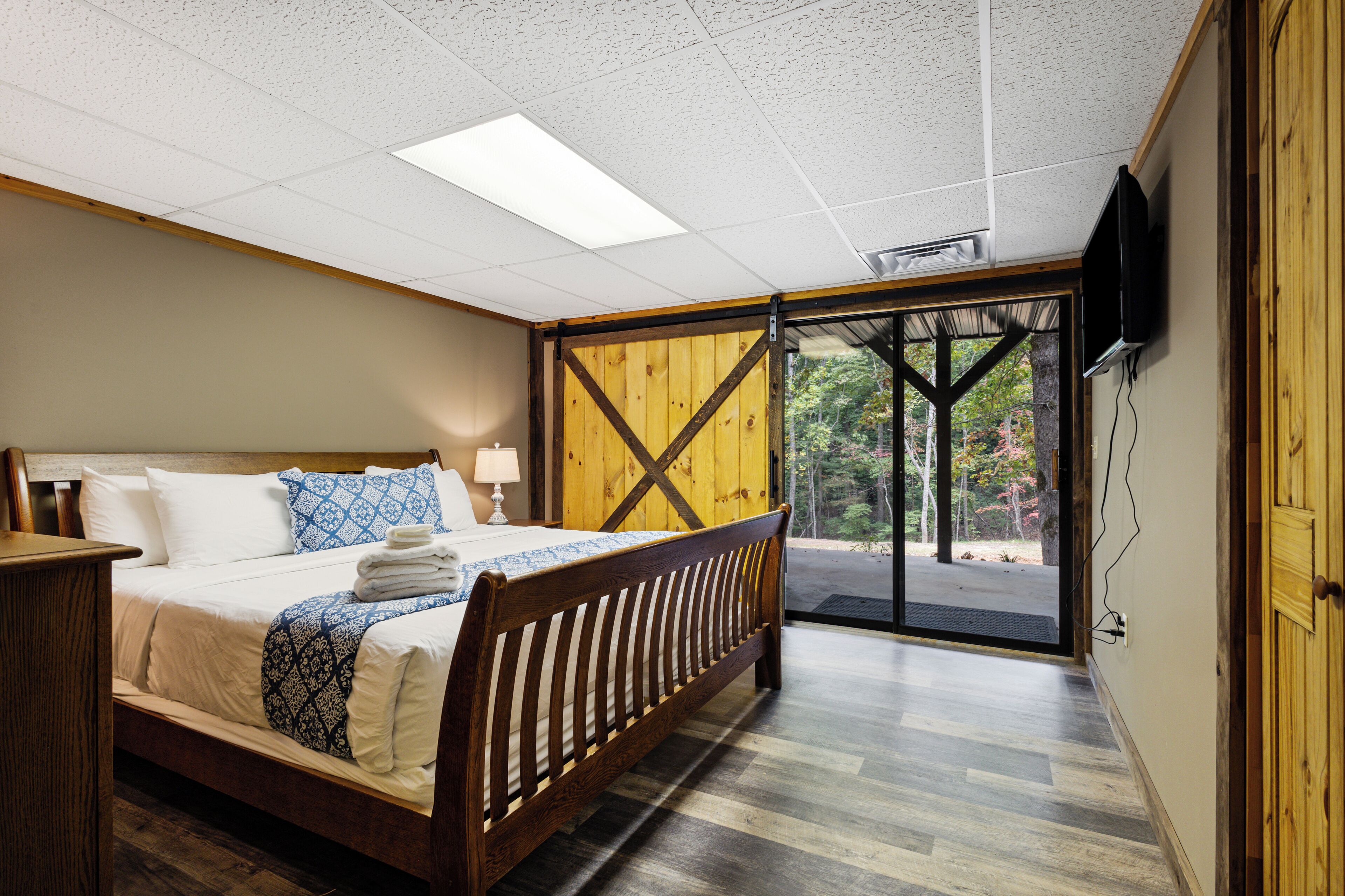 A bedroom with a wooden bed, a nightstand, a lamp, and a TV mounted on the wall.