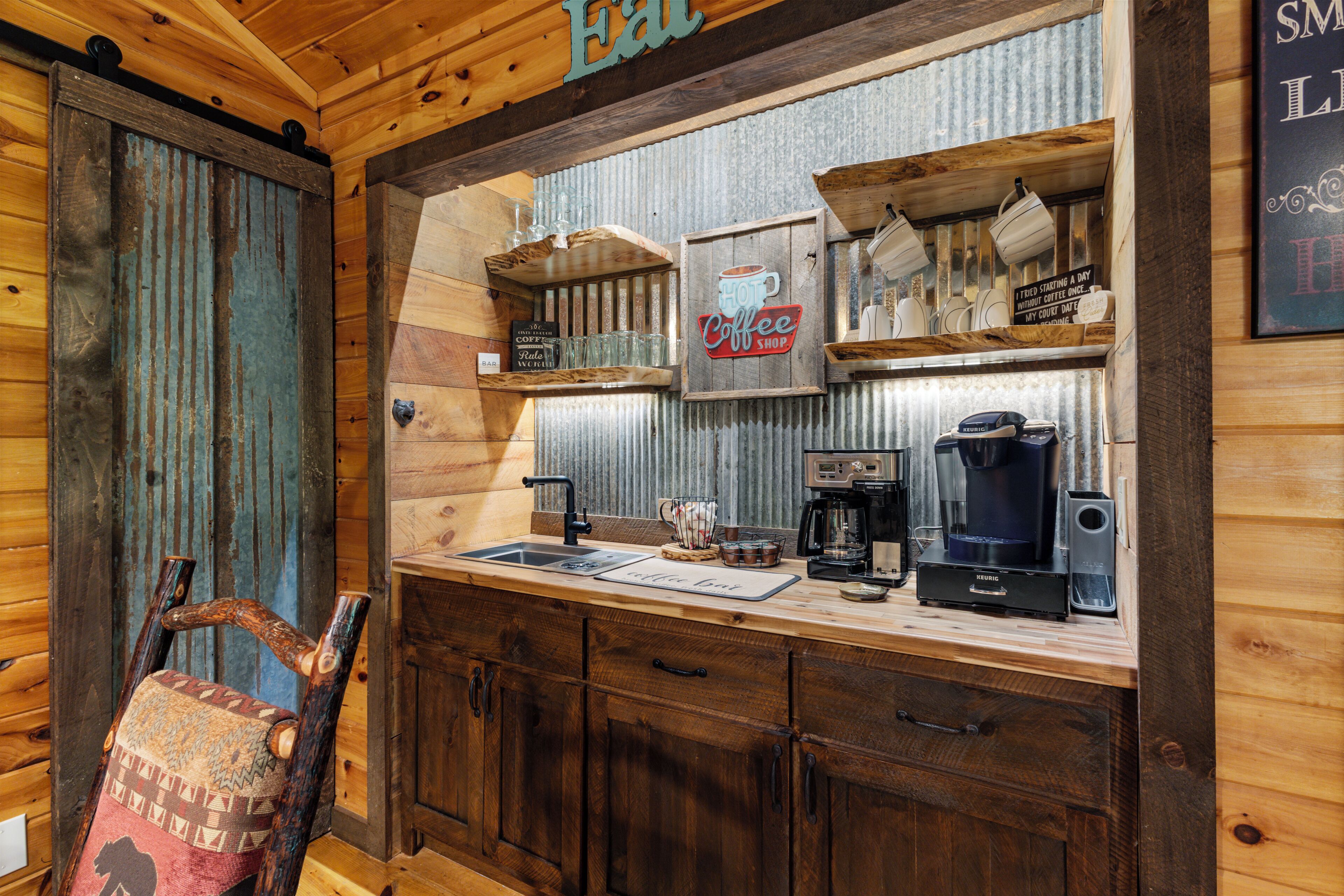 A rustic kitchen with wooden cabinets, a coffee shop sign, and a coffee maker.