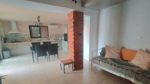 A living room with a sofa, a brick pillar, and a kitchen area with a dining table and chairs. - Bel Appartement, au Calme. Animaux de Compagnie Acceptés ! (Corbère-les-Cabanes)
