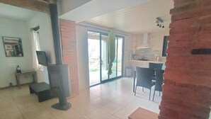 A spacious living area with a large window, a fireplace, a dining table, and a kitchen area. - Bel Appartement, au Calme. Animaux de Compagnie Acceptés ! (Corbère-les-Cabanes)