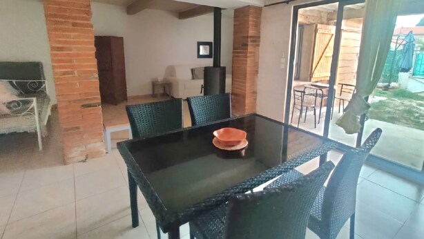 A dining area with a glass table and chairs, a brick wall, and a view of the backyard. - Bel Appartement, au Calme. Animaux de Compagnie Acceptés ! (Corbère-les-Cabanes)
