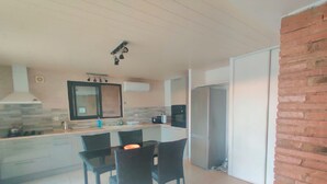 A modern kitchen with a dining area, featuring a large island, black chairs, and a refrigerator. - Bel Appartement, au Calme. Animaux de Compagnie Acceptés ! (Corbère-les-Cabanes)