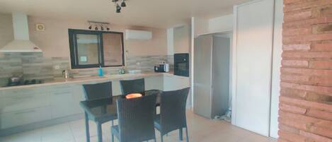 A modern kitchen with a dining area, featuring a large island, black chairs, and a refrigerator.