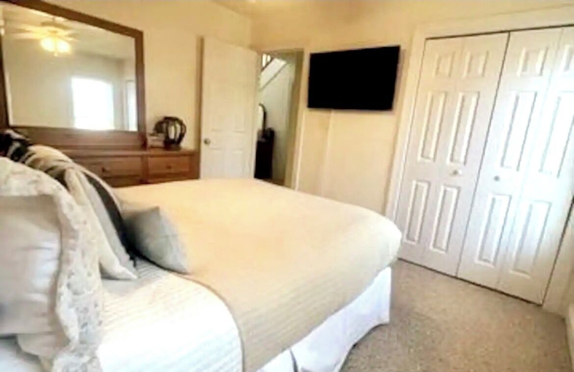 Un dormitorio con cama, cómoda, espejo, televisor y armario.