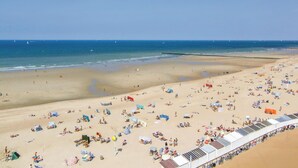Una amplia playa con numerosas tumbonas y sombrillas, un cielo despejado y un mar tranquilo.