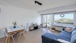 Una sala de estar moderna con comedor, sofá, televisor y vista al mar.