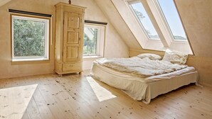 Une chambre avec un plafond en pente, un lit, une armoire et deux fenêtres.