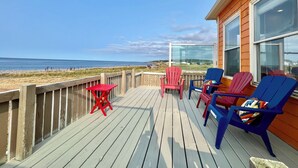 A wooden deck with a view of the beach, featuring red and blue Adirondack chairs and a small red table. - Escape to your private oasis in our ocean front home with breathtaking views.  (Grand Bank)