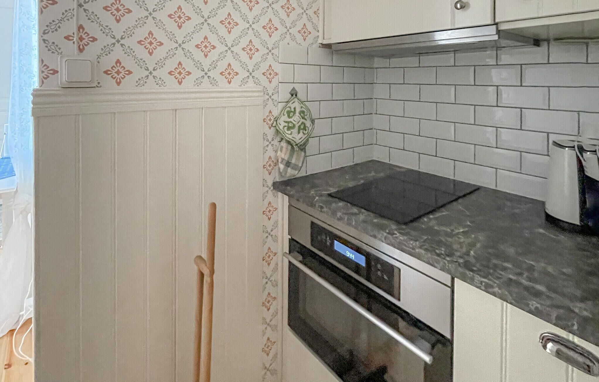 Una cocina con armarios blancos, encimera negra y salpicadero de azulejos blancos.