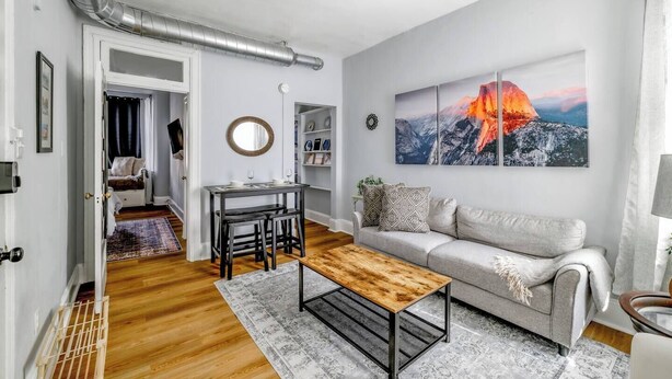 A modern living room with a wooden coffee table, a grey sofa, and a painting of a mountain landscape. - Perfect Adams Morgan Location! Charming & Historic (Washington)
