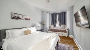 A bedroom with a large bed, a window seat, a flat-screen TV, and a painting on the wall. - Perfect Adams Morgan Location! Charming & Historic (Washington)