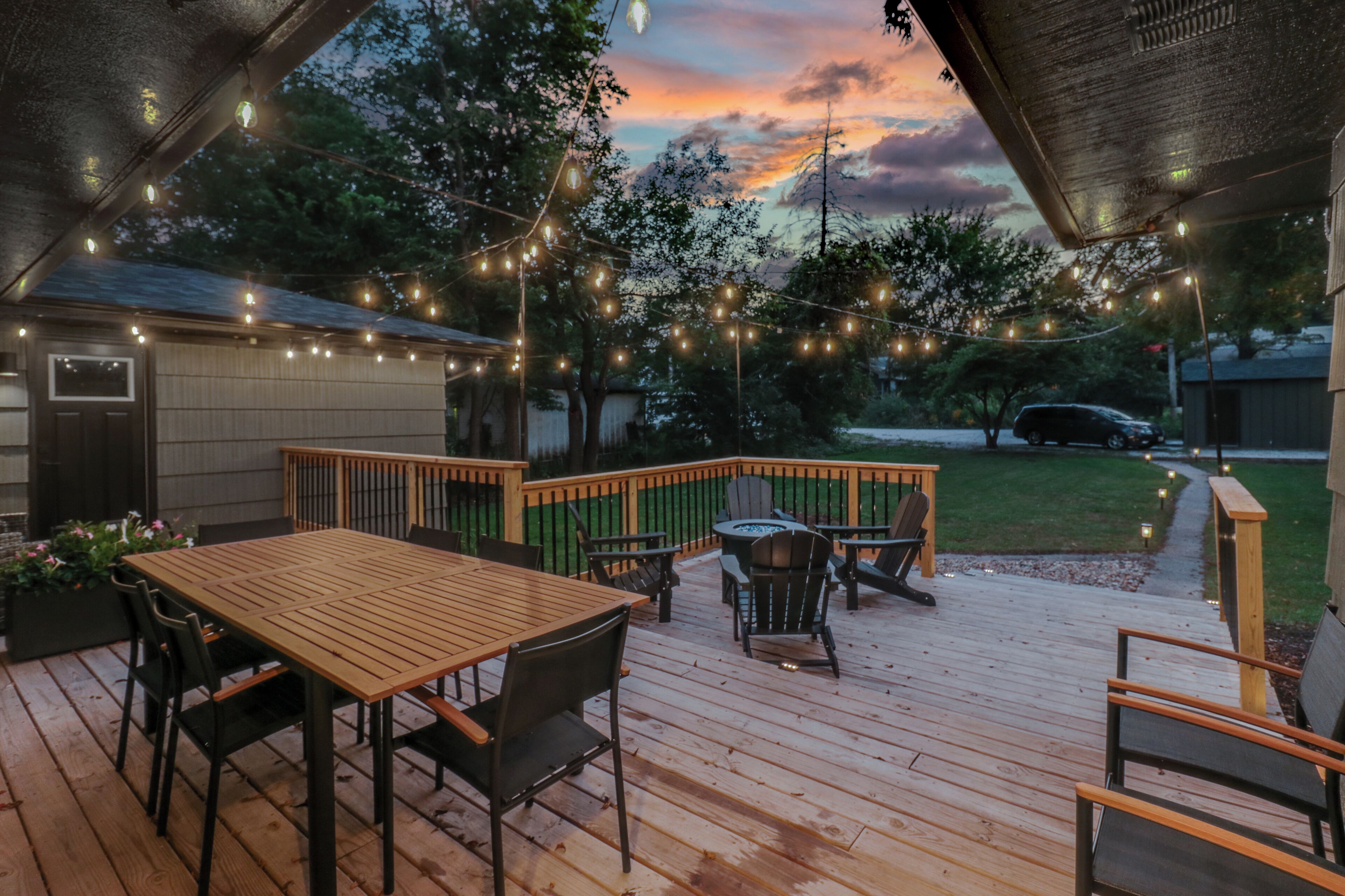 A wooden deck with a table and chairs, surrounded by a wooden fence and string lights.