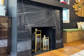 A modern living room with a black marble fireplace, wooden shelves, and a green cushioned bench. - The Normal School House  (Normal)