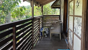 Una terraza de madera con un espacio cubierto, una silla y un muro con paneles decorativos.