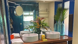 Un baño con dos lavamanos, un espejo, un perchero para toallas y una planta en maceta.