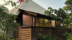 Una cabaña rústica de madera con techo inclinado, rodeada de exuberante vegetación y plantas en flor.
