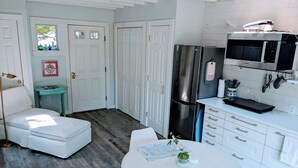 A compact kitchen with white cabinetry, a stainless steel refrigerator, a Bosch microwave, and a small round table with placemats. - Cozy Seaside studio in charming Marblehead with AC, WiFi. Short walk to downtown (Marblehead)