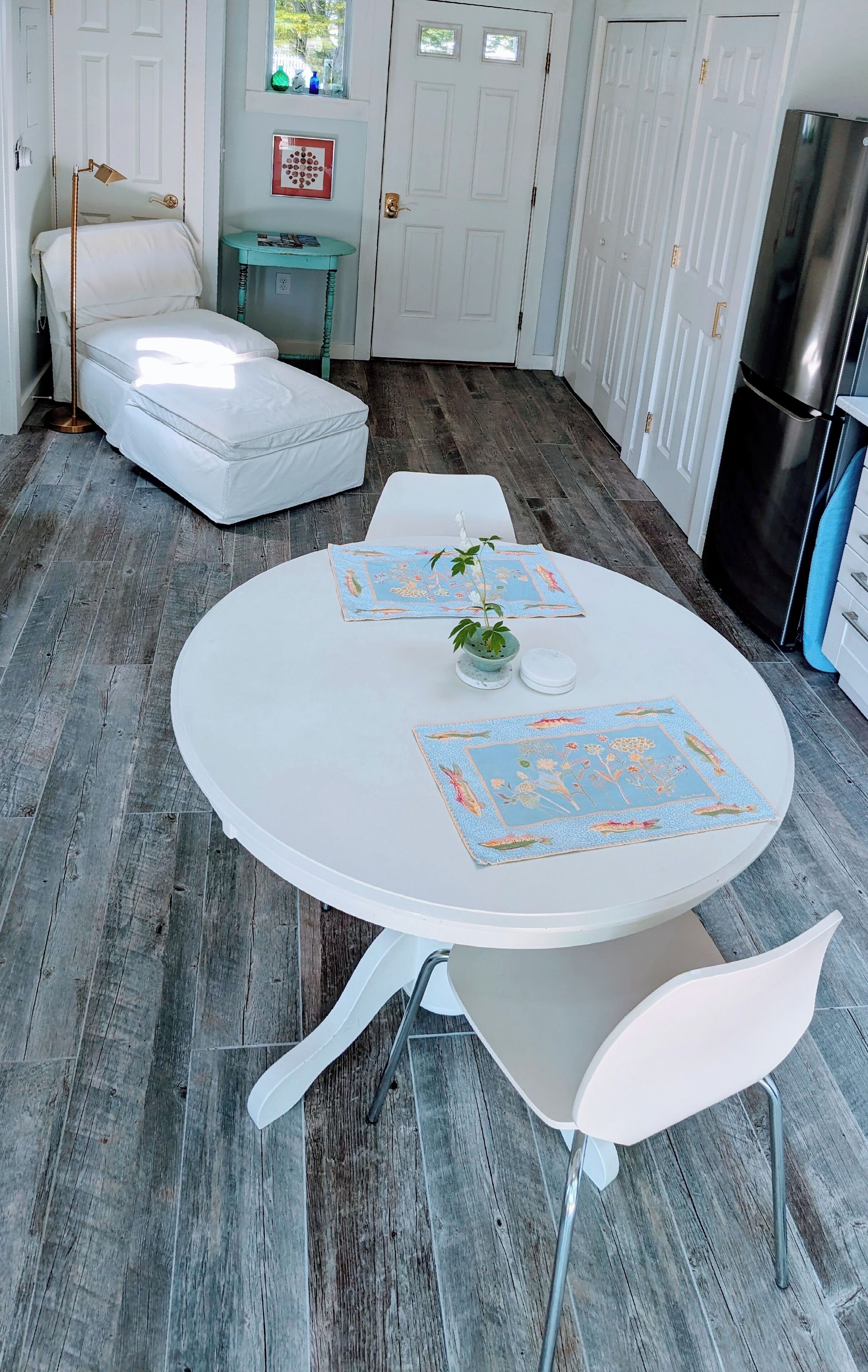 A cozy room with a round white table, two white chairs, a small potted plant, and a decorative mat.