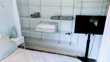 A bedroom with a bed, a TV mounted on the wall, and a built-in shelving unit with folded towels and blankets.