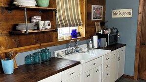 A kitchen with white cabinets, a wooden countertop, a sink, a clock, and a window with striped curtains. - Cozy studio in enjoyable Gypsum with AC, WiFi (Gypsum)