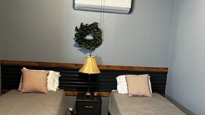 A room with two beds, a small table, a bench, a wall-mounted air conditioner, and a ceiling fan. - Cozy studio in enjoyable Gypsum with AC, WiFi (Gypsum)