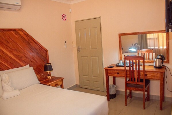A hotel room with a wooden headboard, a bed with white linens, a desk with a chair, a lamp, and a coffee maker.