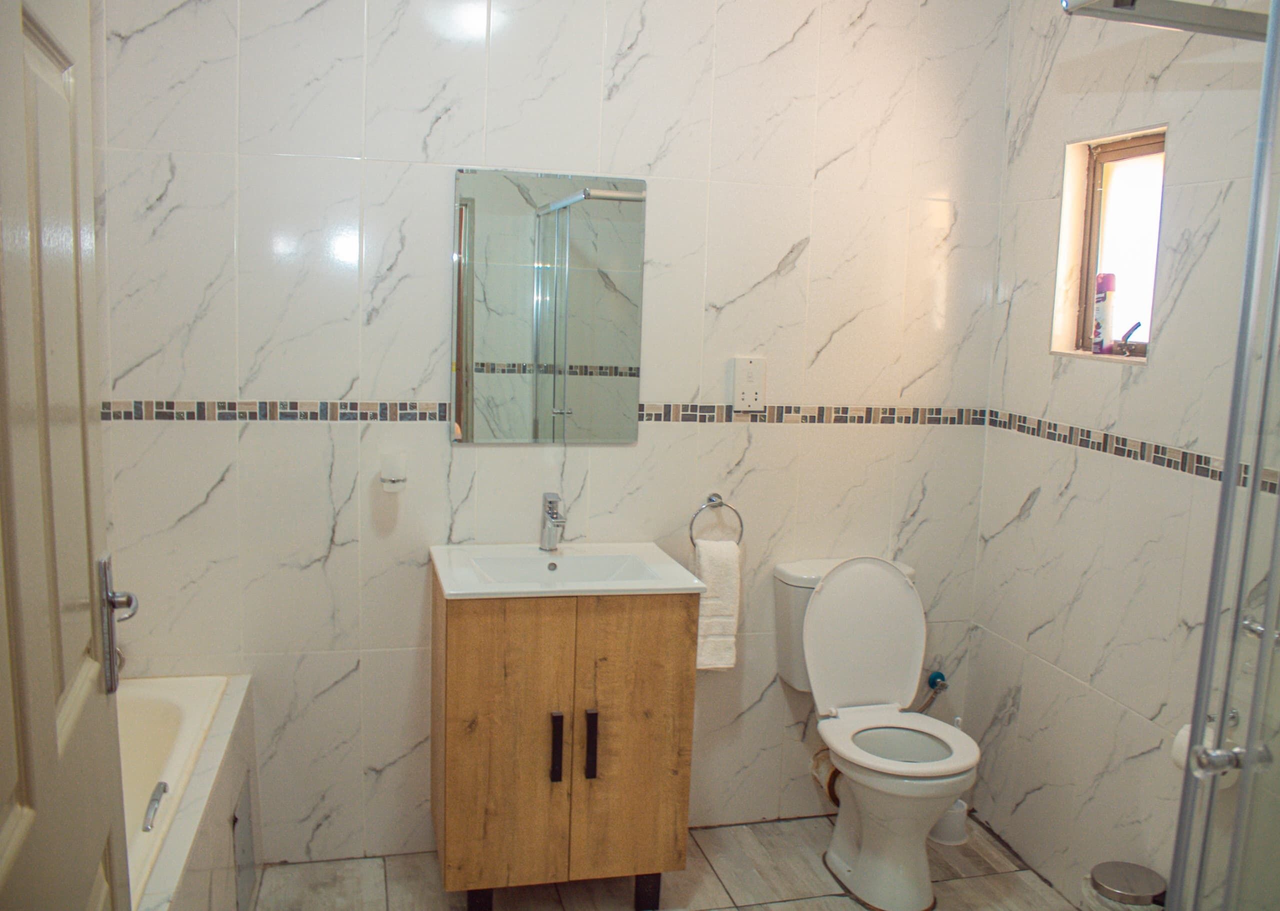 Une salle de bain avec un mur en marbre, un meuble en bois, un lavabo, des toilettes et un espace douche.