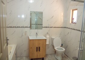 Une salle de bain avec un mur en marbre, un meuble en bois, un lavabo, des toilettes et un espace douche.
