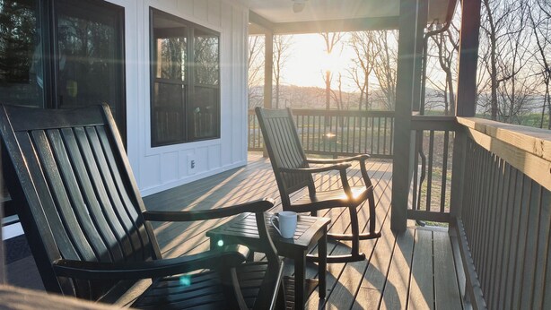 A covered outdoor seating area with two chairs and a table, overlooking a landscape with trees and a distant view. - Secluded New Cottage, Minutes From Sunset Marina Overlooking Pendergrass Creek (Byrdstown)
