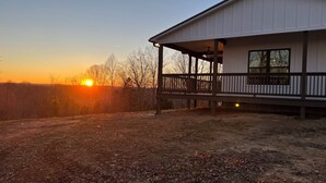 A building with a covered porch and a view of the sunset. - Secluded New Cottage, Minutes From Sunset Marina Overlooking Pendergrass Creek (Byrdstown)