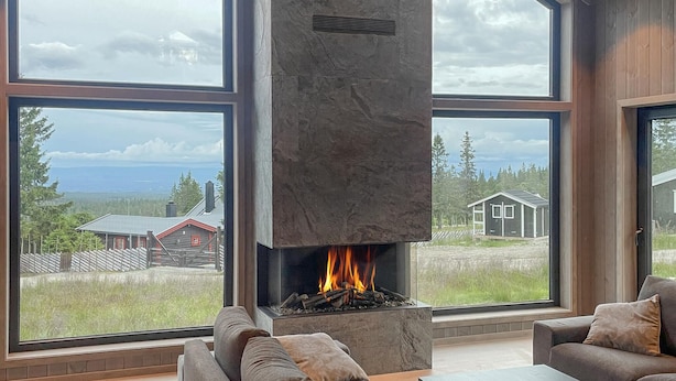 Una sala de estar moderna con chimenea, ventanas amplias y vistas a una casa y árboles.