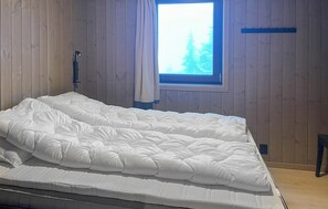 Un dormitori amb un llit, una finestra i parets de fusta.