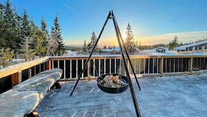 Una terraza cubierta de nieve con una silla colgante y un pozo de fuego.