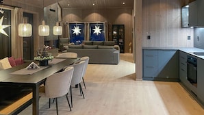 Una cocina moderna con zona de comedor, que presenta piso de madera, un sofá gris y lámparas colgantes con bombillas en forma de estrella.
