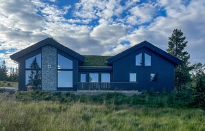 Una casa moderna de dos pisos amb grans finestres, façana de pedra i un paisatge amb gespa.
