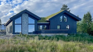 Una casa moderna de dos pisos con amplios ventanales, fachada de piedra y techo verde.
