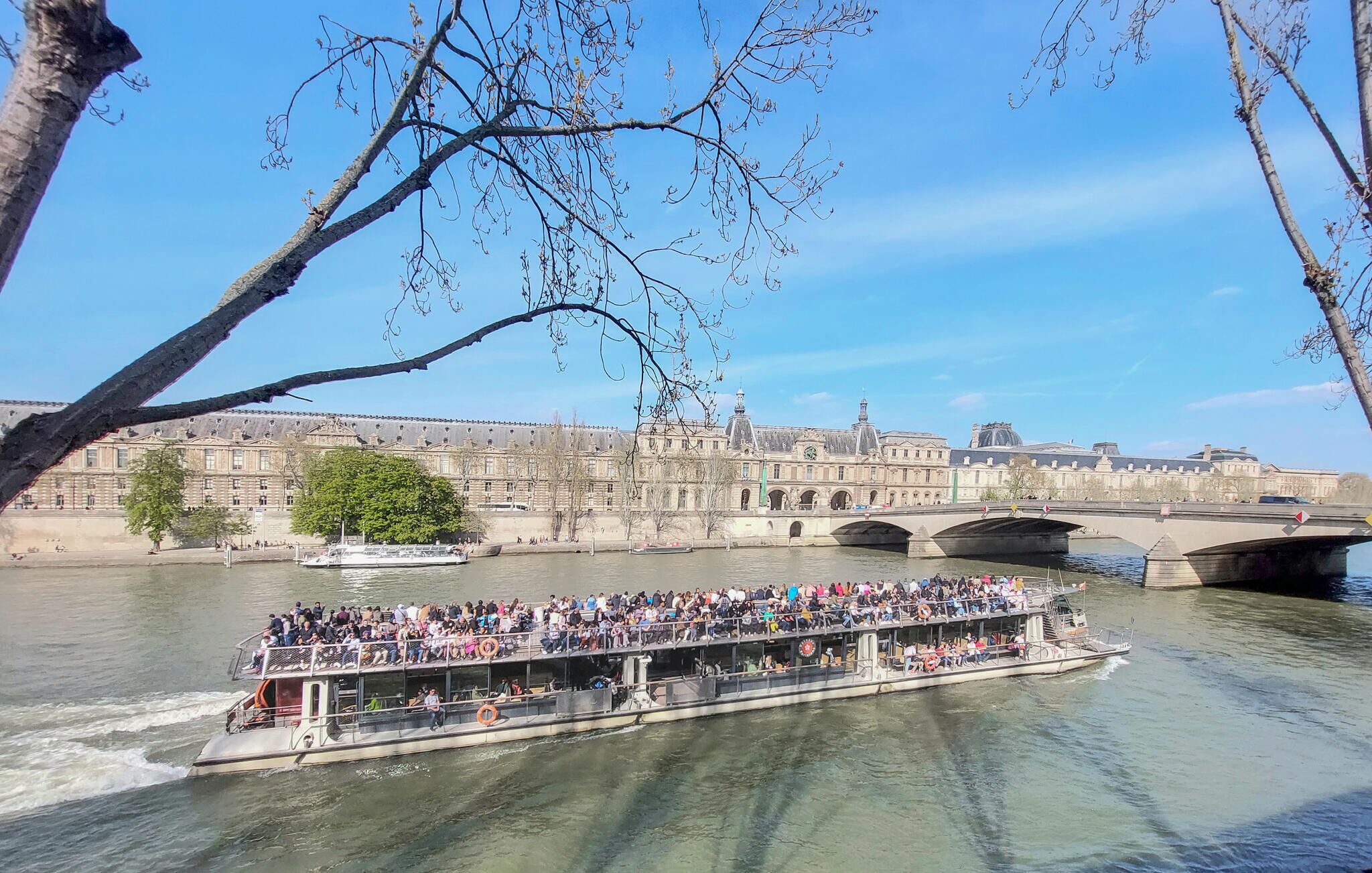 A river cruise boat with passengers, a bridge, and historic buildings in the background.
